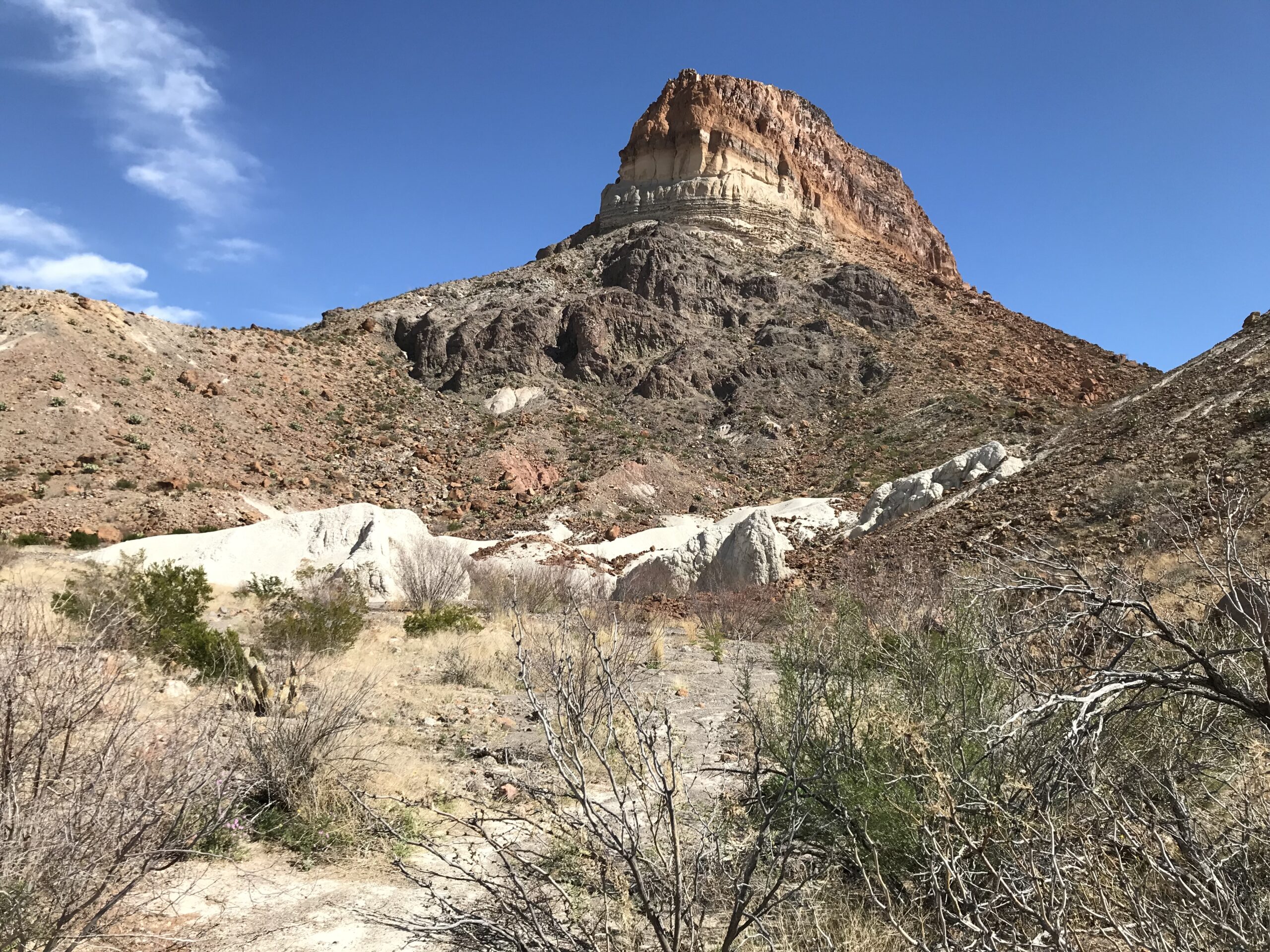Cerro Castellan, a layered volcanic peak with red-brown, tan, and cream rock bands, rising against a blue sky in Big Bend National Park