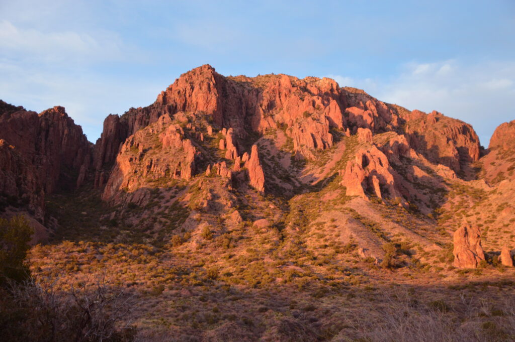 Sunset light glows across the rugged red-rock peaks of the Chisos Mountains, seen from the Chisos Basin campground in Big Bend National Park