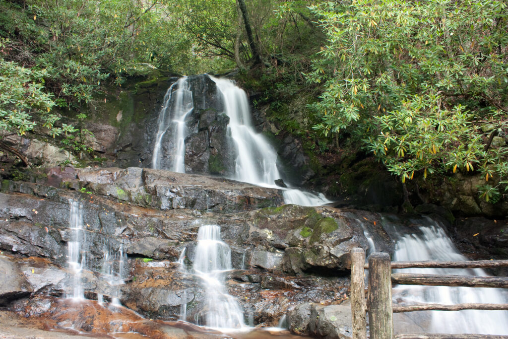Laurel Falls cascading over layered rock formations in Great Smoky Mountains National Park, with a wooden trailside fence in the foreground