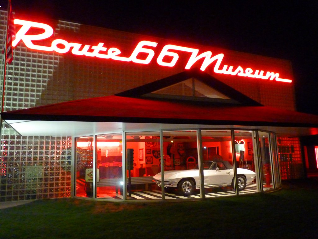 Route 66 Museum in Clinton, Oklahoma at night with red neon sign and glass front displaying a classic car inside