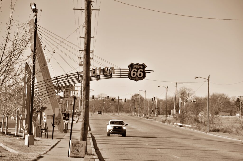 Sepia-toned image of a car driving under the Route 66 arch in Tulsa, Oklahoma near the Route 66 Historical Village