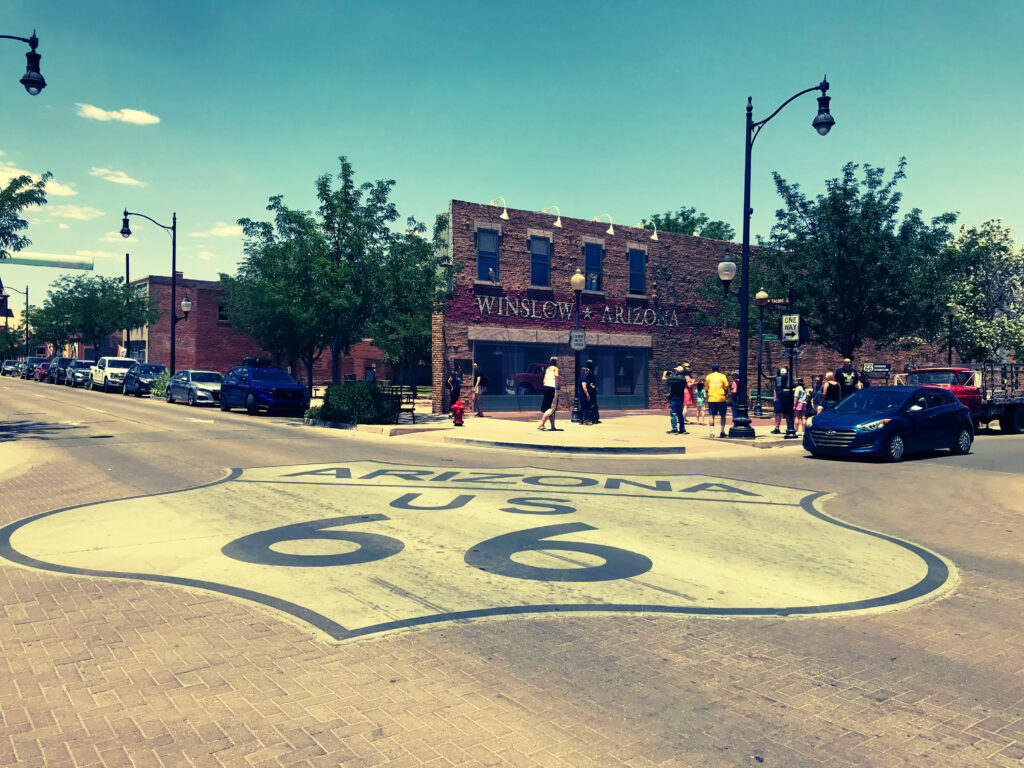 Route 66 road shield painted on the street at Standin on the Corner in Winslow Arizona with visitors and historic brick buildings in the background