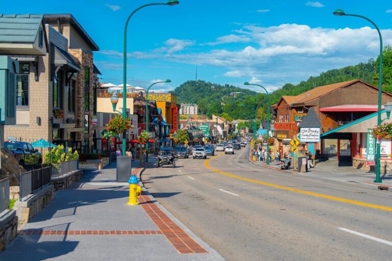 A busy street in downtown Gatlinburg lined with shops and restaurants, including Ole Smoky Candy Kitchen, with mountains in the background