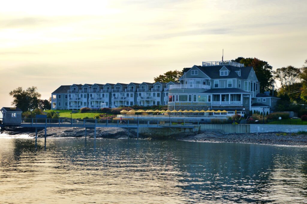The Bar Harbor Inn, a waterfront hotel with white porches and gray shingle siding, at sunset in Bar Harbor, Maine