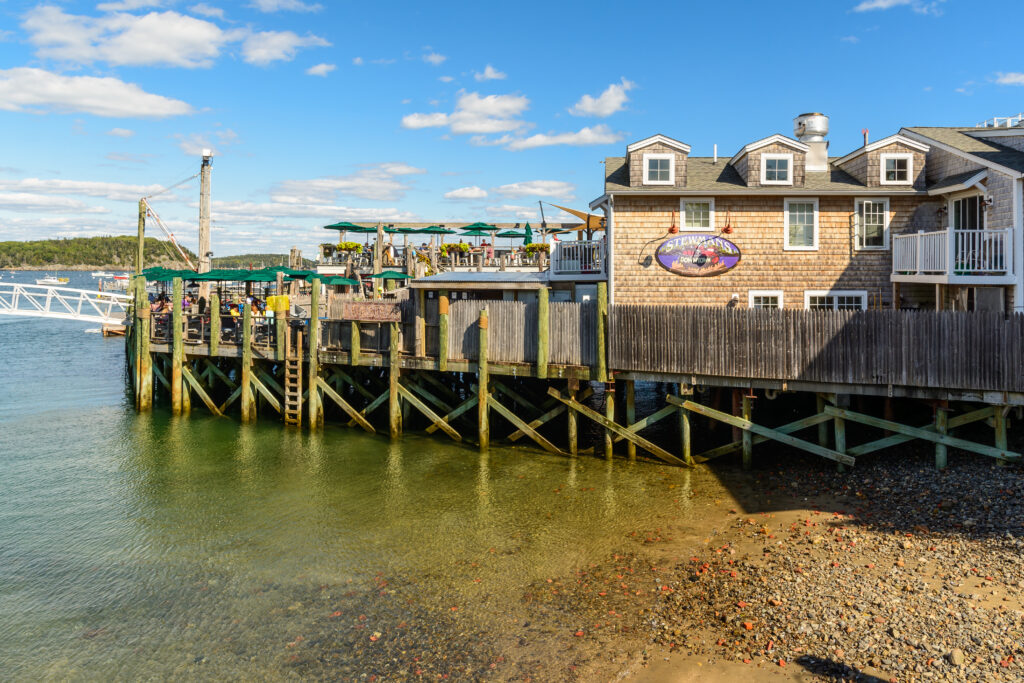 A waterfront lobster restaurant on a wooden pier in downtown Bar Harbor, Maine, with outdoor dining and boats in the harbor