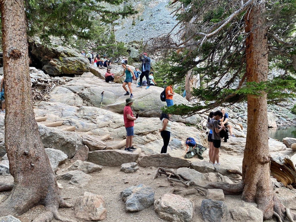 A crowded rocky shoreline at Emerald Lake in Rocky Mountain National Park, with hikers waiting to take photos