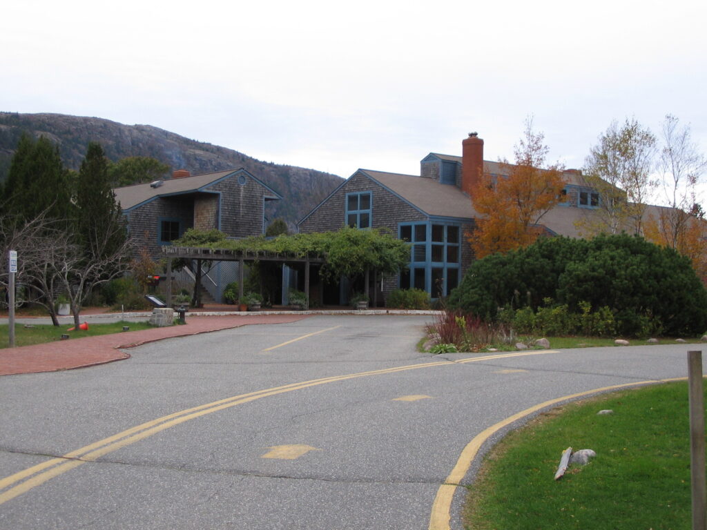 The Jordan Pond House restaurant and gift shop, a shingle-style building with blue trim, set against a mountain backdrop in Acadia National Park