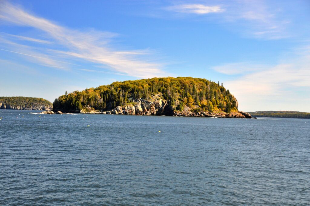 One of the Porcupine Islands in Frenchman Bay, Maine, showing its sloped and cliff-cut glacial shape covered in evergreen and fall-colored trees