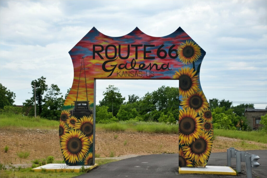 A colorful arched sign reading "Route 66 Galena Kansas, US" painted with sunflowers and a vintage truck silhouette, spanning a road