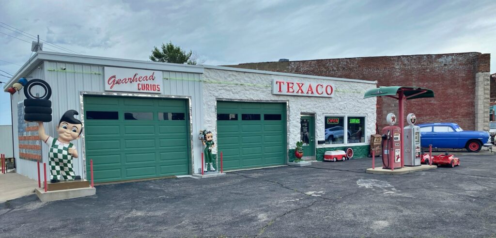 The Gearhead Curios shop in Galena, Kansas, with a large Texaco sign, a giant statue of a man in uniform, a Big Boy statue, and a vintage blue car parked out front
