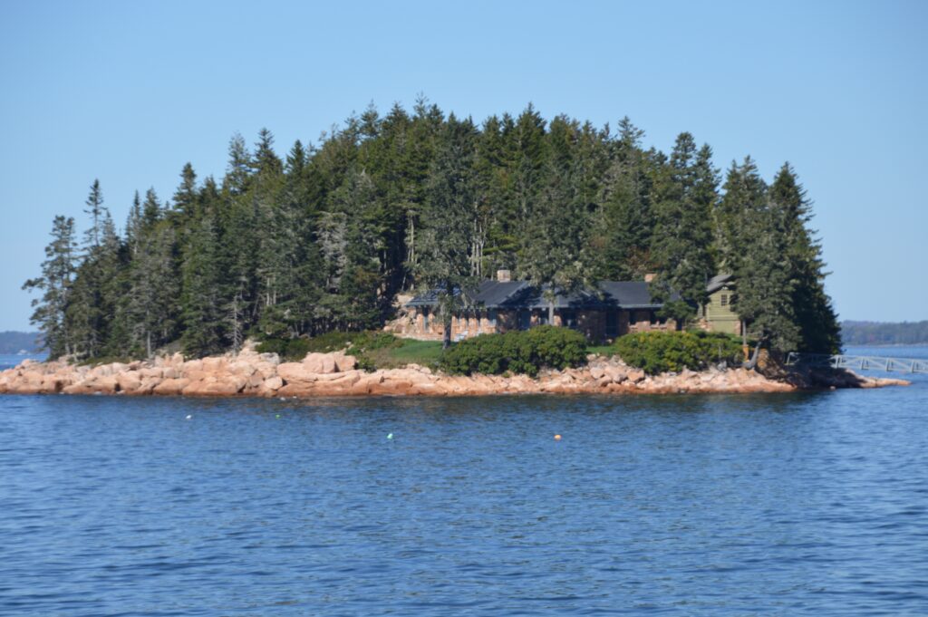 A private island with a stone cottage among pine trees on rocky red granite shoreline in Frenchman Bay, Maine