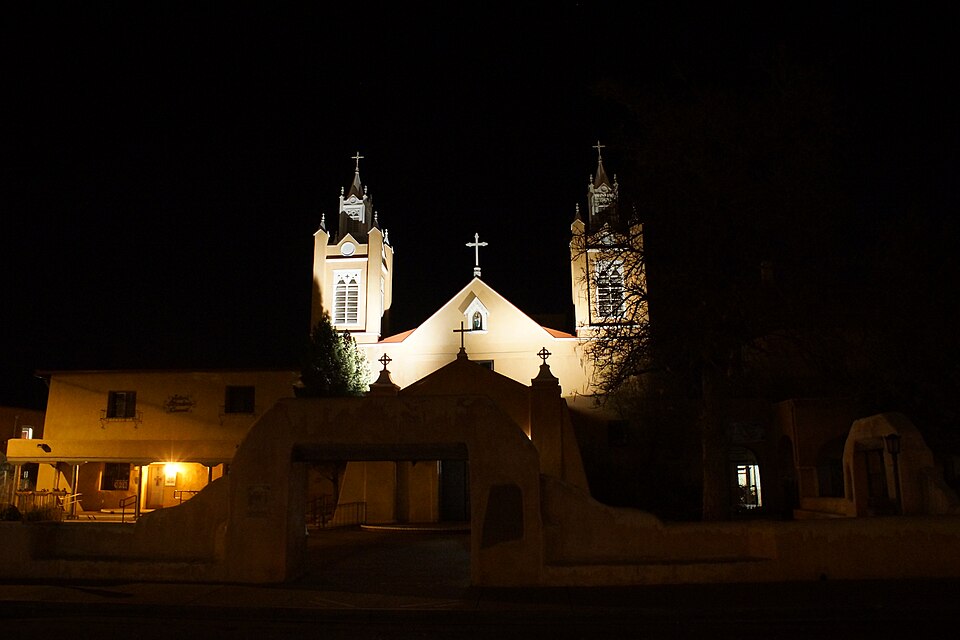 San Felipe de Neri Church in Old Town Albuquerque illuminated at night, its twin bell towers lit against a dark sky