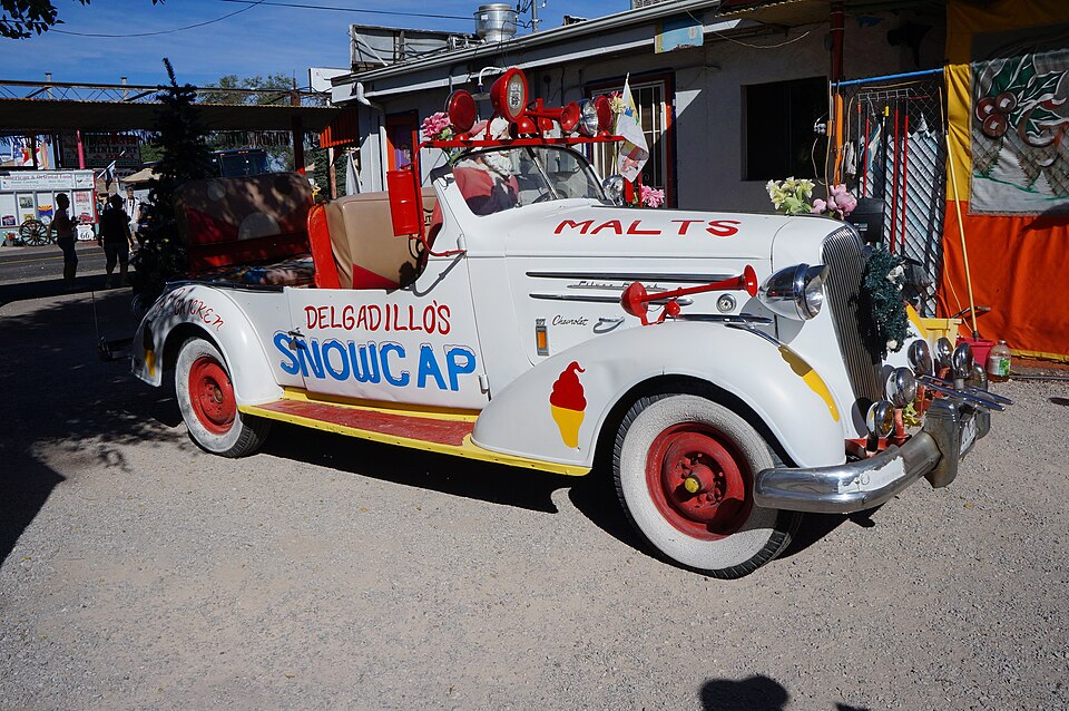 A vintage white convertible car decorated with 'Delgadillo's Snowcap' and 'Malts' signage, parked outside a roadside shop in Seligman, Arizona