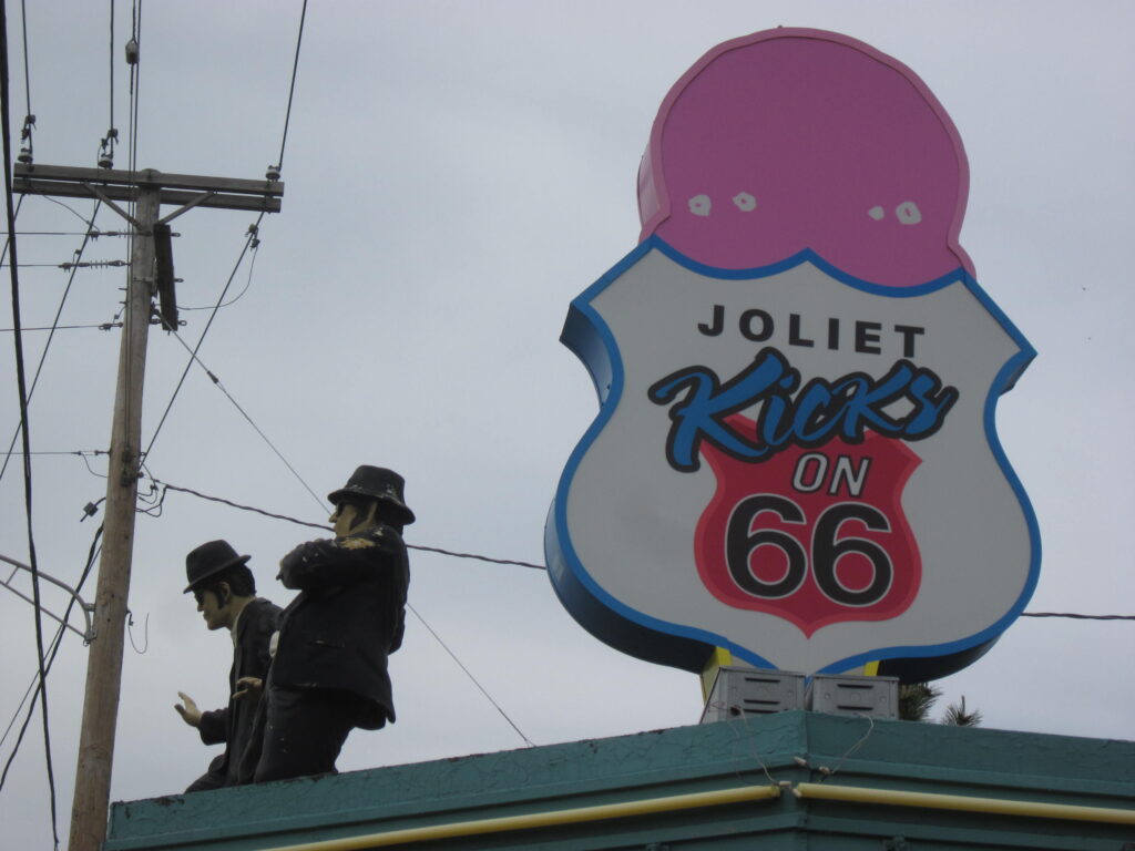 Close-up of Blues Brothers figures on a rooftop beside a "Joliet Kicks on 66" ice cream cone sign