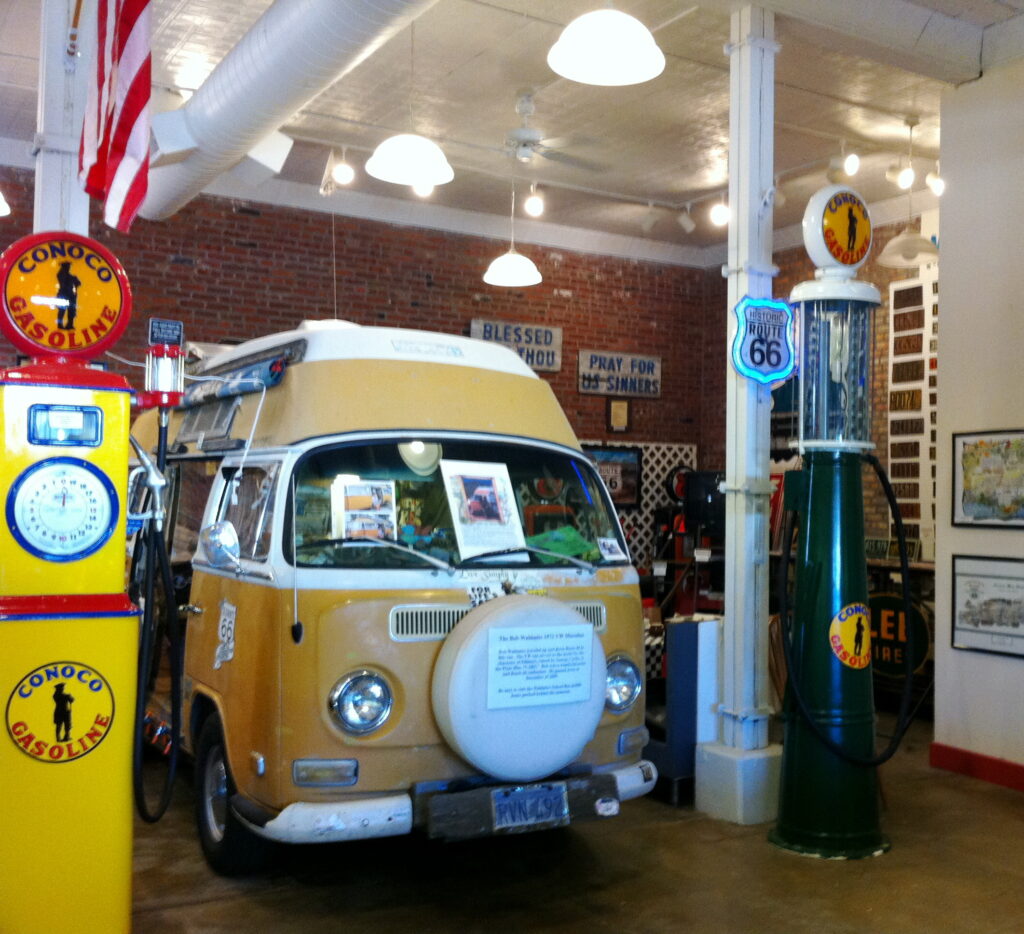 Bob Waldmire's yellow and white 1972 VW Microbus on display inside the Route 66 Hall of Fame and Museum, surrounded by vintage gas pumps and Route 66 memorabilia