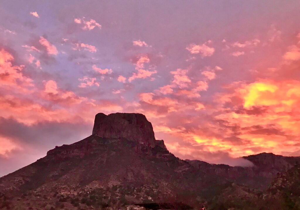 Vivid pink and orange clouds streak the sky at sunrise above Casa Grande in the Chisos Basin at Big Bend National Park