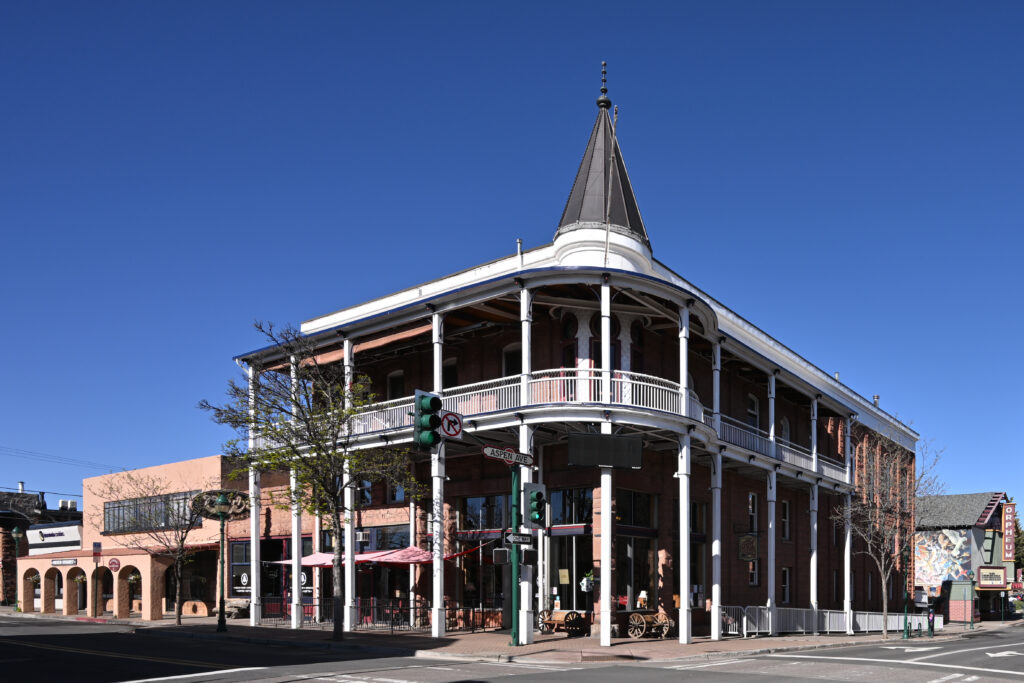 The Weatherford Hotel in downtown Flagstaff, a Victorian brick building with a wraparound balcony and a tall corner turret, under a clear blue sky