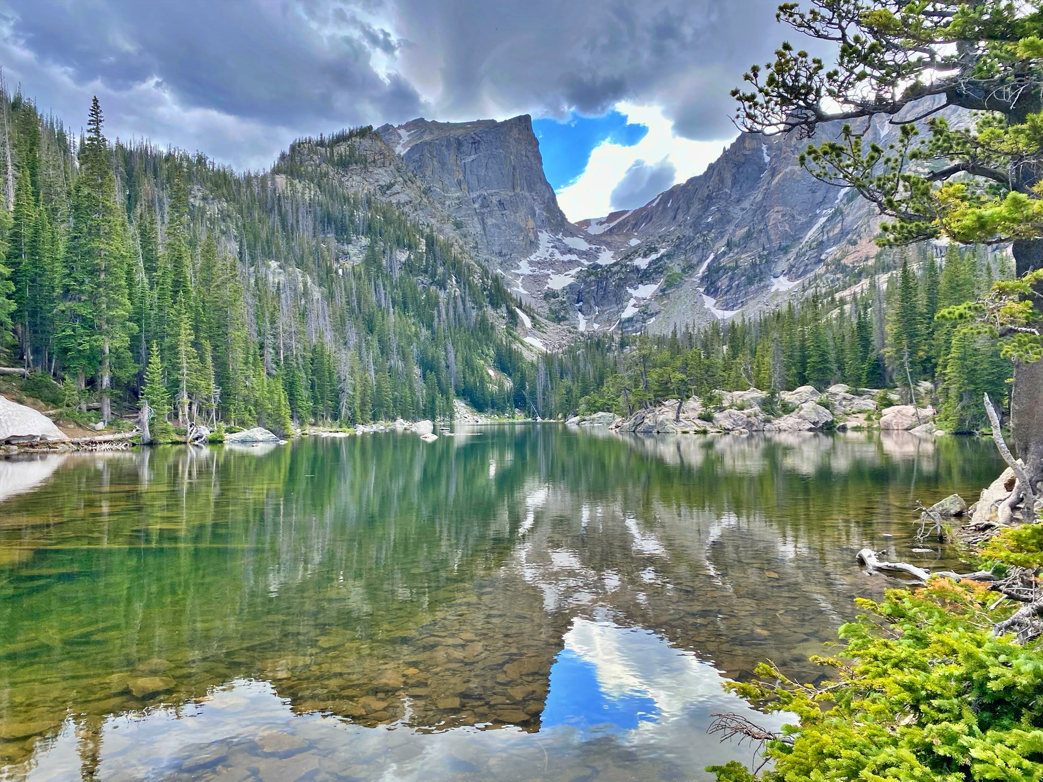 Dream Lake with crystal-clear water reflecting the jagged peaks and pine forest of Rocky Mountain National Park under a partly cloudy sky