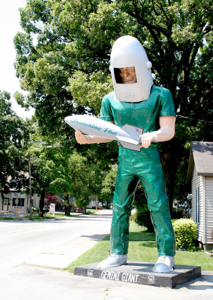 The Gemini Giant, a 28-foot fiberglass astronaut statue in a green jumpsuit and silver helmet, holding a rocket labeled "Launching Pad," standing outside a Route 66 restaurant