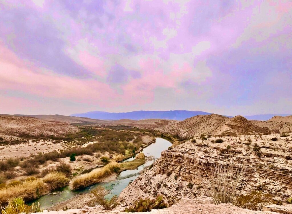 The Rio Grande winds through desert hills beneath a pastel pink and purple sky along the Hot Springs Trail in Big Bend National Park