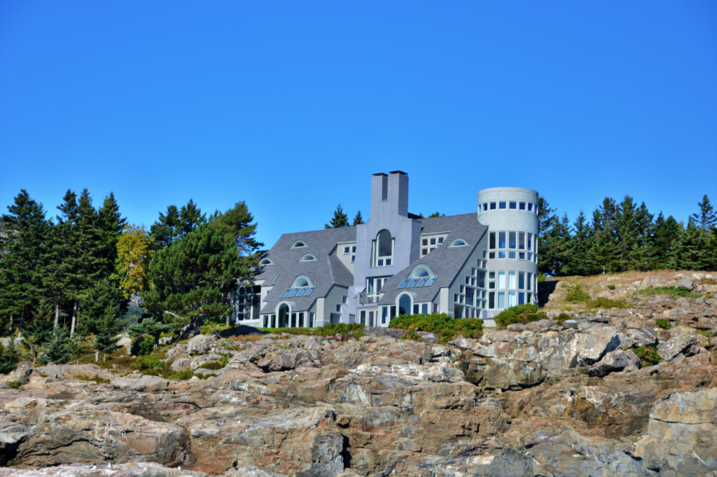 A large shingle-style coastal mansion on a rocky cliff near Bar Harbor, Maine, surrounded by pine trees