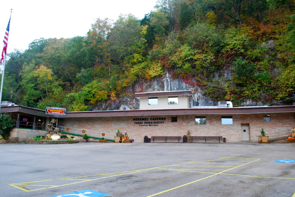 The entrance to Meramec Caverns, a brick building with "Meramec Caverns Jesse James Hideout" painted on the wall, set against a limestone bluff with autumn foliage