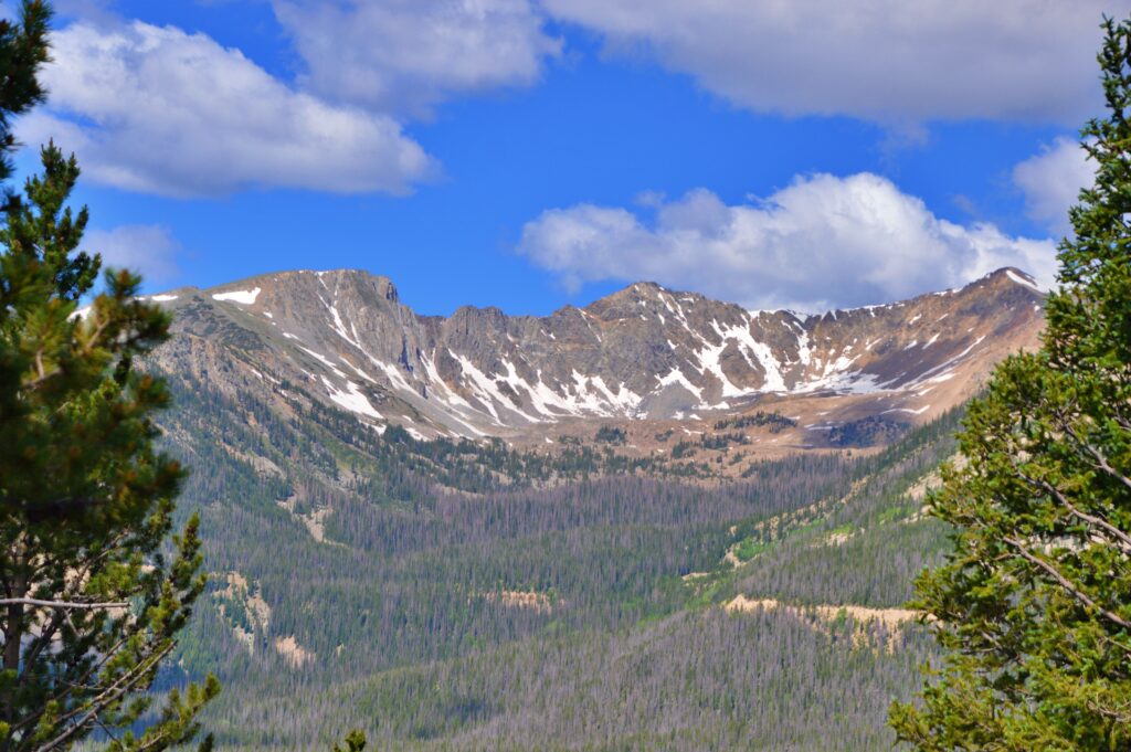 A rugged mountain range bathed in warm evening light, with layered ridgelines and scattered clouds, seen from a distance across open terrain