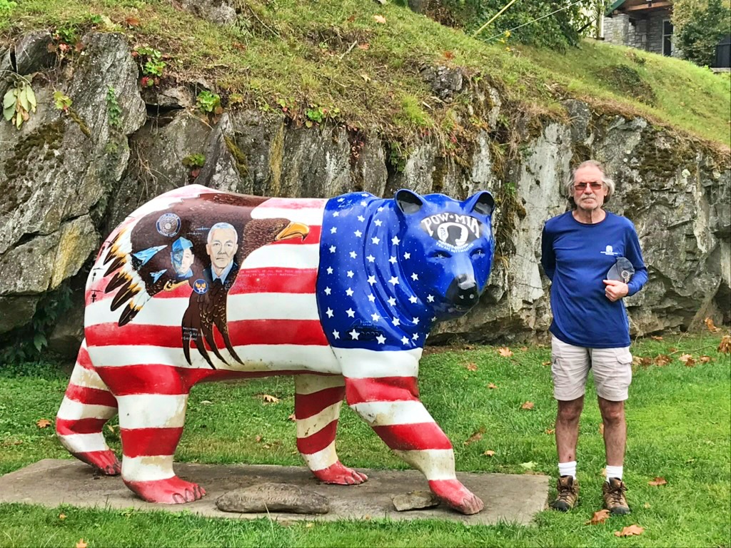 A man standing beside the Patriot Bear statue, a bear painted in an American flag design with a POW/MIA emblem, in downtown Cherokee, North Carolina