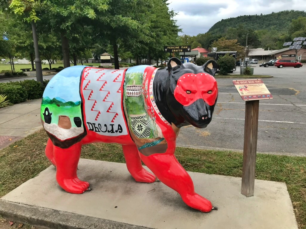 A red and black bear statue painted with pottery, landscape scenes, and geometric patterns, part of Cherokee's Great Bear Hunt trail
