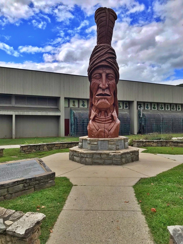 large wooden carved bust of Sequoyah wearing a turban, mounted on a stone pedestal outside a building in Cherokee, North Carolina
