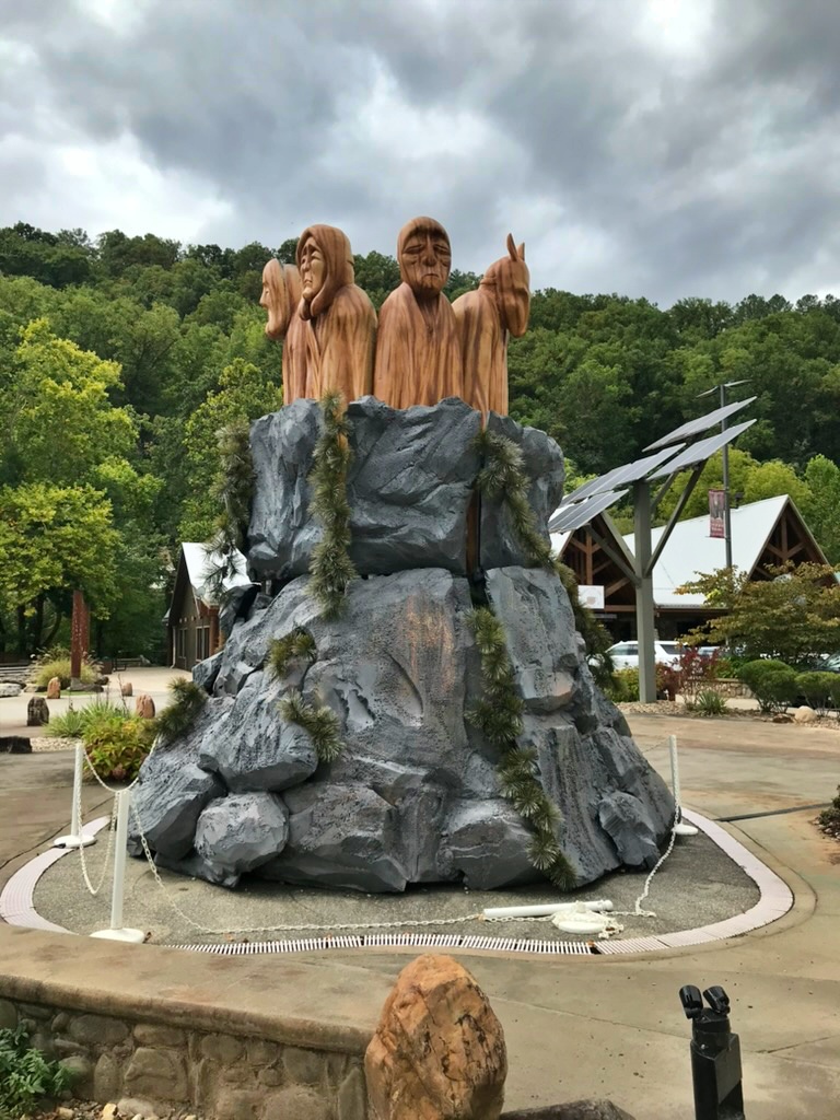 A sculpture of robed wooden figures representing the seven Cherokee clans, rising from an artificial stone outcrop in downtown Cherokee