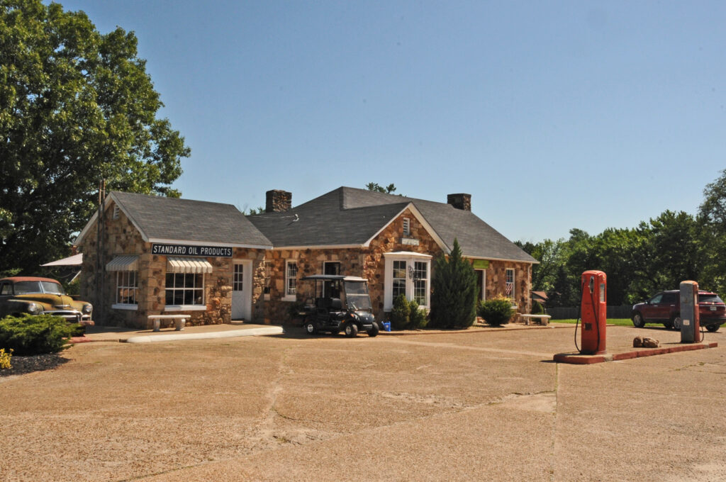 The stone building of the Wagon Wheel Motel and gas station in Cuba, Missouri, with vintage cars, a golf cart, and old red gas pumps out front