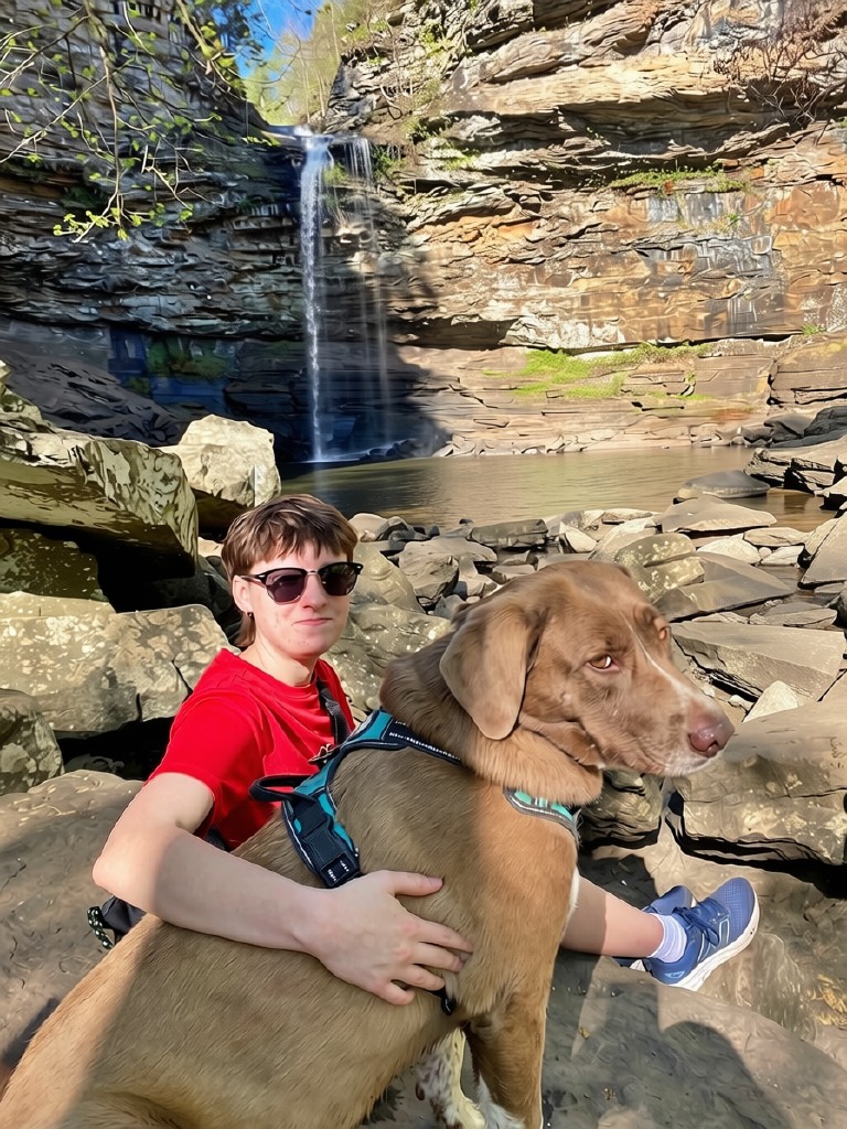 Woman with her dog sitting at the base of Cedar Falls waterfall at Petit Jean State Park, Arkansas