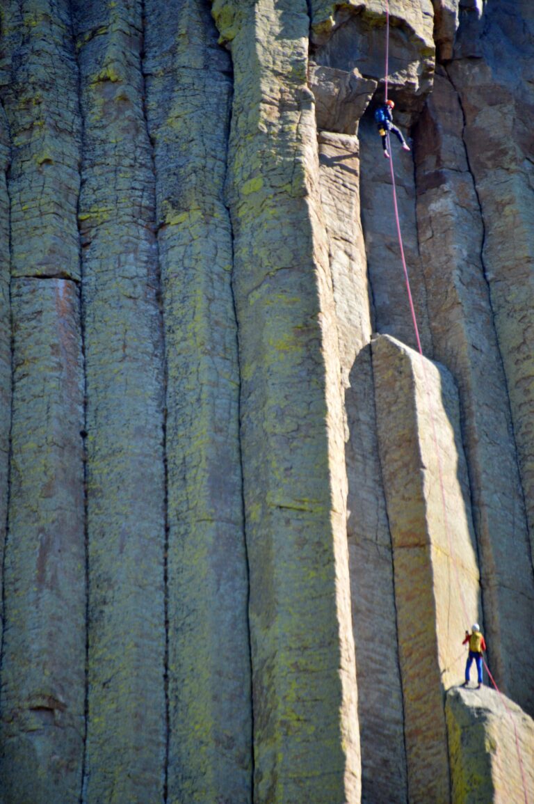 Two rock climbers rappelling down the columnar basalt face of Devils Tower on ropes