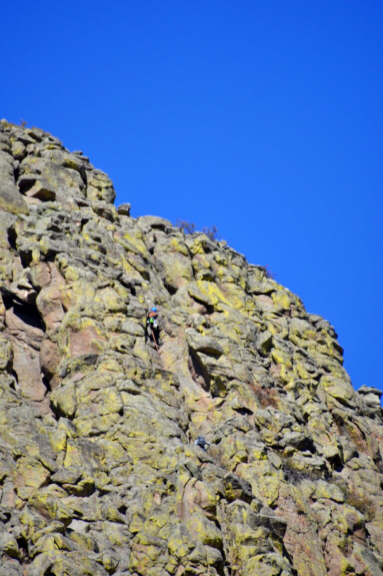 Two rock climbers ascending a crack on the back side of Devils Tower, dwarfed by the massive columnar rock face