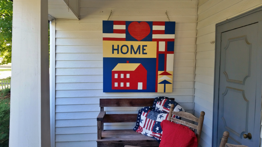 Patriotic 'Home' quilt square with a red house design hanging on a porch in Stone County, Arkansas