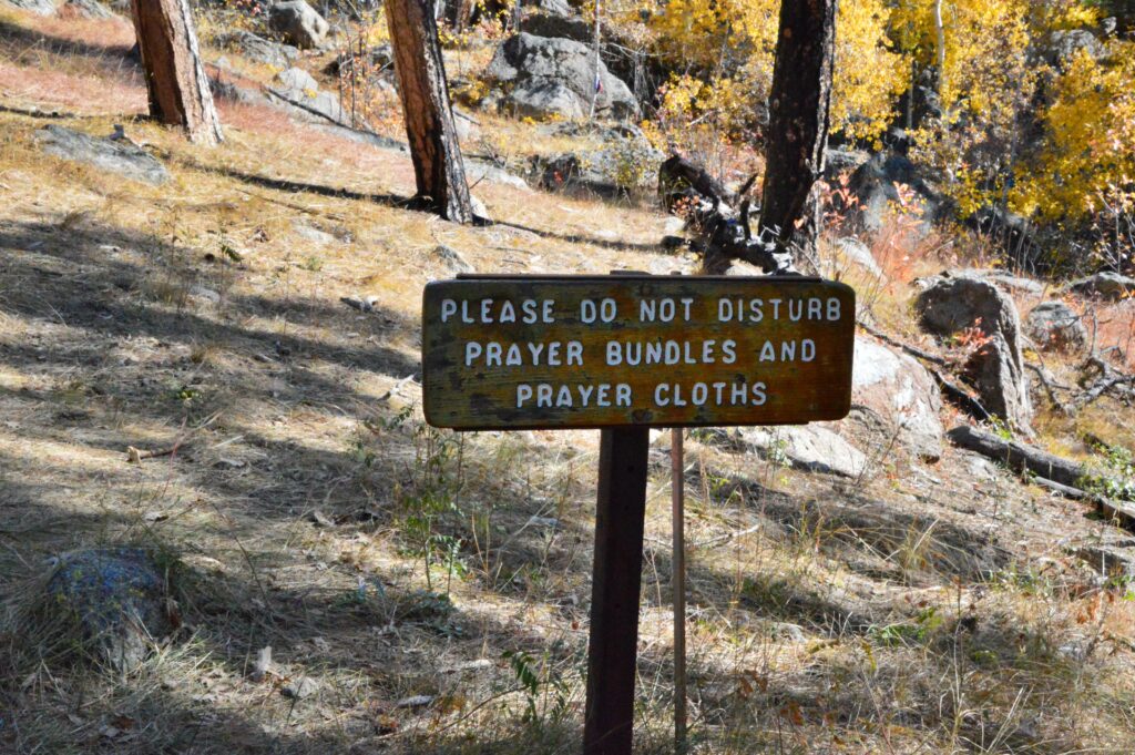 Wooden trail sign at Devils Tower reading 'Please do not disturb prayer bundles and prayer cloths