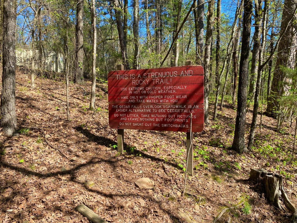 Wooden trail warning sign at Petit Jean State Park cautioning hikers about the strenuous, rocky Cedar Falls Trail
