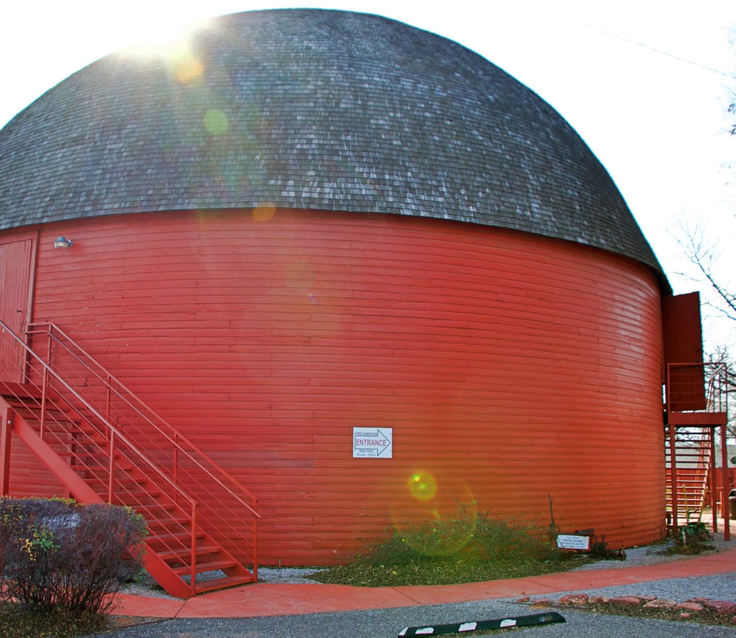 Arcadia Round Barn in Oklahoma, a large red circular wooden barn with a steep domed roof and exterior staircase, photographed in daylight along Route 66.