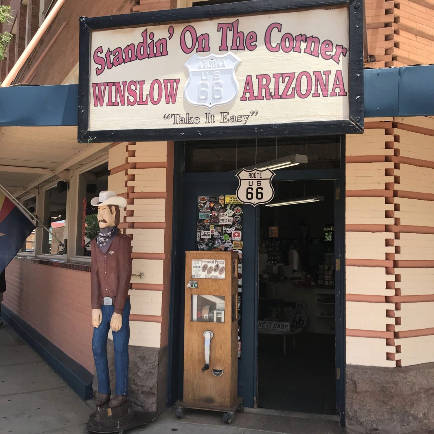 Standin on the Corner sign and entrance in Winslow Arizona with Route 66 sign and statue outside the storefront