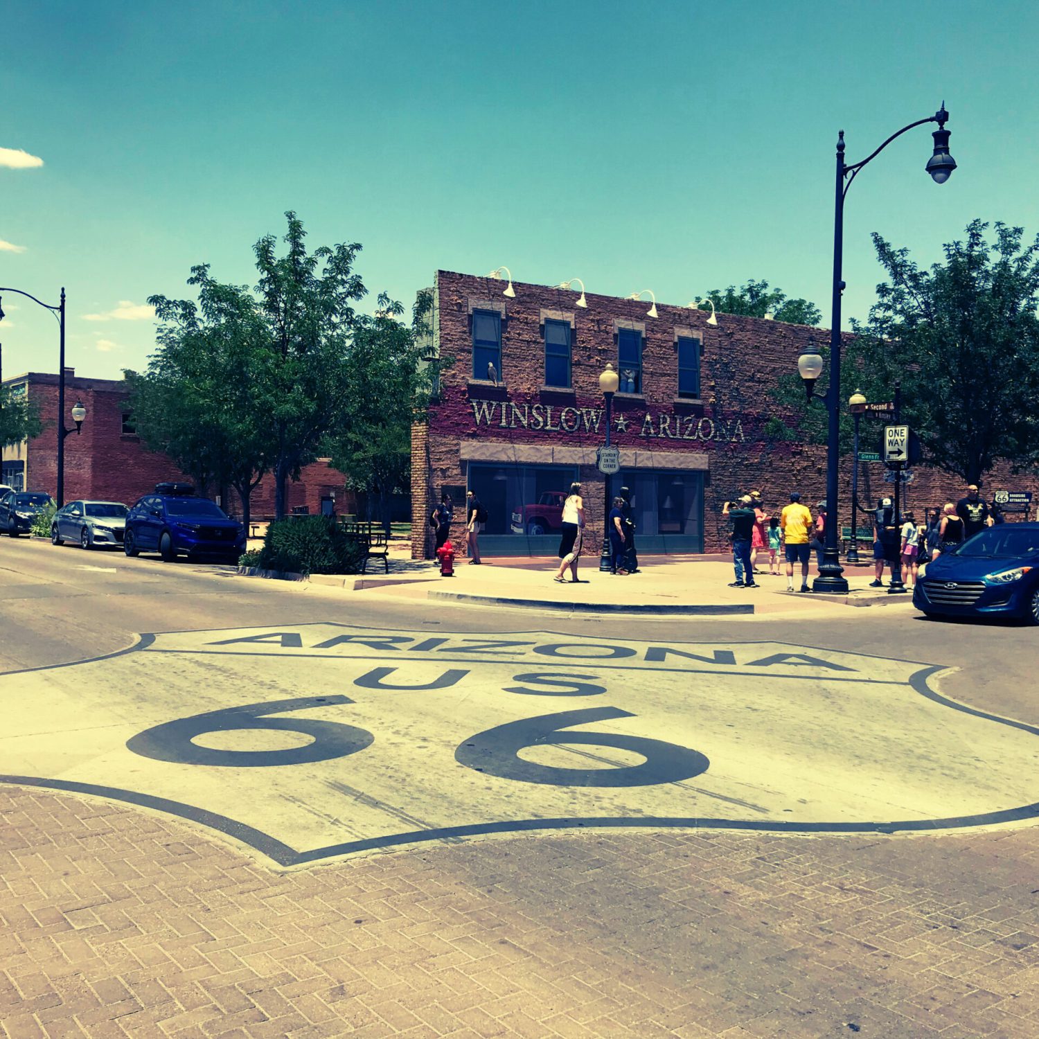 Route 66 road shield painted on the street at Standin on the Corner in Winslow Arizona with visitors and historic brick buildings in the background